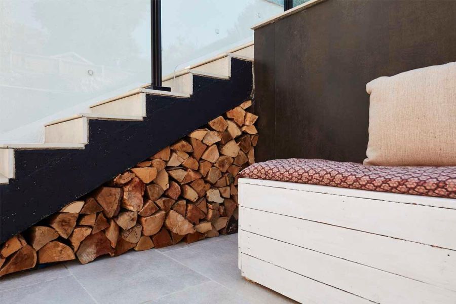 Seating area with DesignClad external cladding and Gea Porcelain Paving, with staircase used as storage for wooden logs underneath.