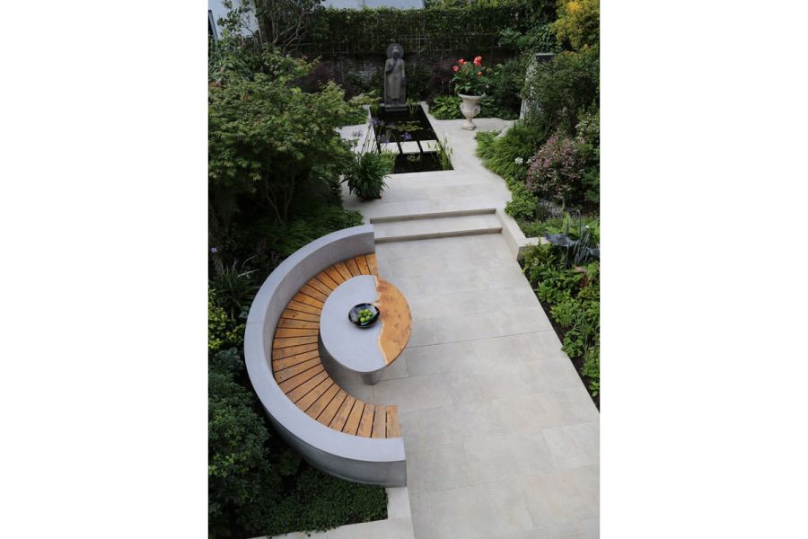 Semi-circular seating area that looks over Gea Porcelain Paving patio with water feature and modern statue at the back.