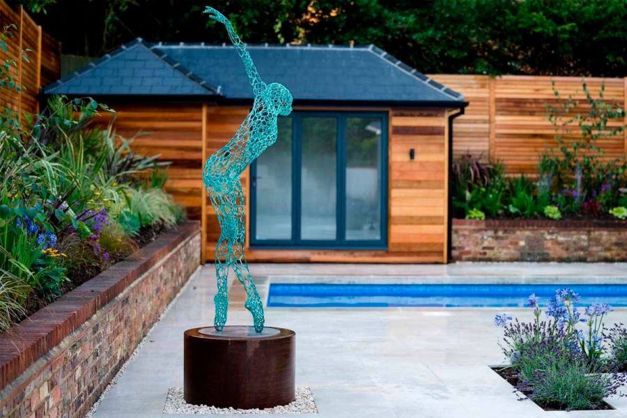 Body-shaped, blue garden statue as the focal point of a modern garden featuring a swimming pool paved around with Gea porcelain.