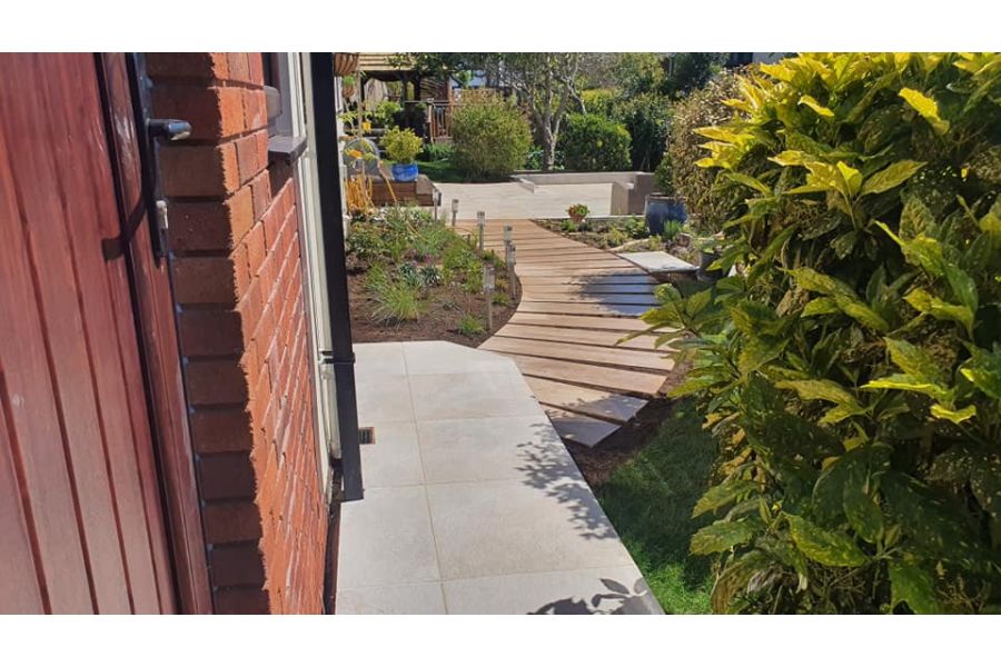 Gea Porcelain Paving garden path leading to a larger paved area that also features soft-landscaping and garden furniture.