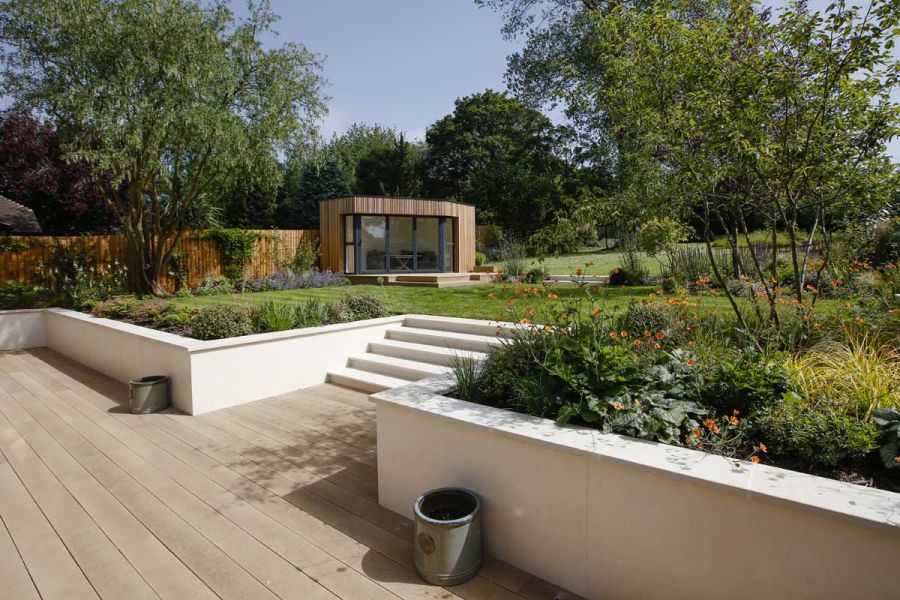 Wide white steps descend between flank walls from large sloping lawn to Golden Oak Millboard decking. By Heartwood Garden Design.