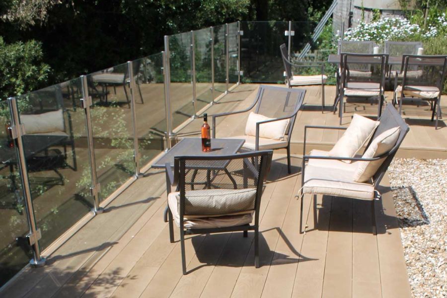 Garden furniture sits on Golden Oak Millboard decking with glass railings built by Outerspace Creative Landscaping.