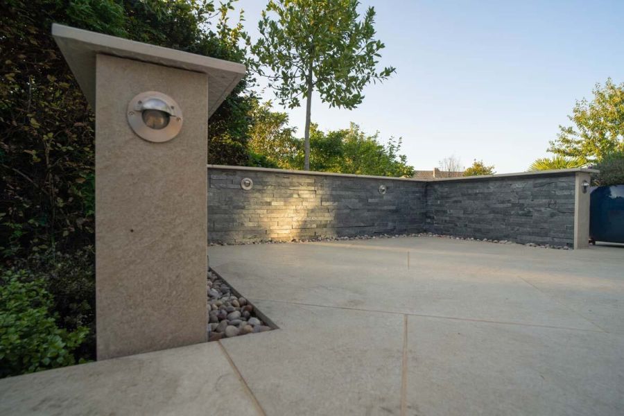 Stone-clad wall, with wide, pencil-round Golden Stone Porcelain coping, enclosing expanse of matching large format paving.