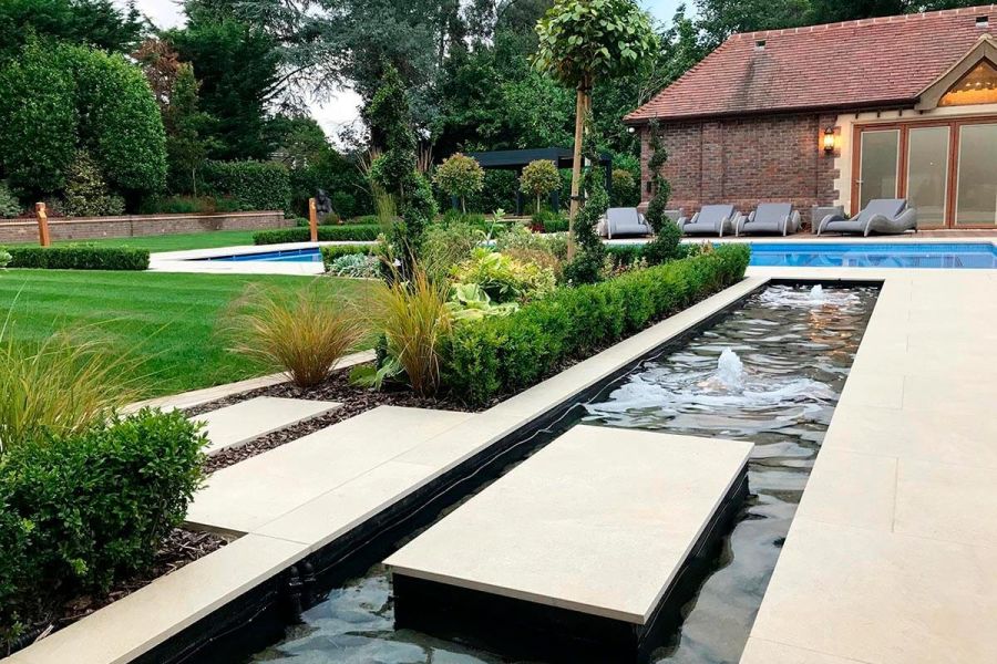 Long rectangular pond with fountains. Golden Stone Porcelain stepping stone provides access across pool to lawn from patio.