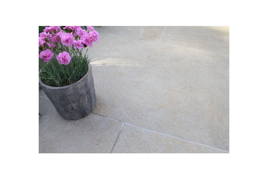 A round planter growing carnations stands on Golden Stone Porcelain paving in running bond pattern, pointed with Norcros grout.