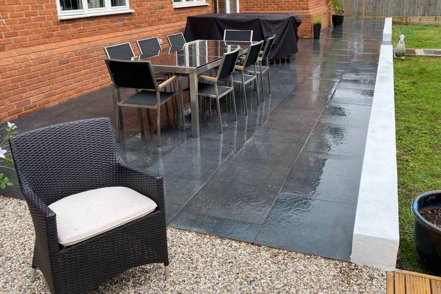 Charcoal porcelain paving slabs with low white wall edge form patios along back of red brick house. Design by Gordius.