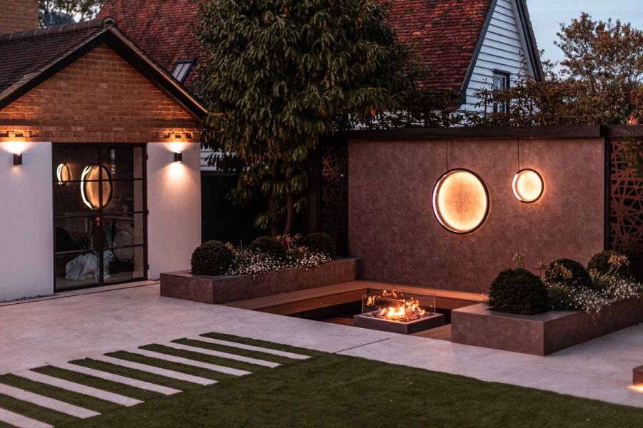Sunken seating with firepit backed by high wall faced with Vulcano Ceniza wall cladding with decorative illuminated circles.
