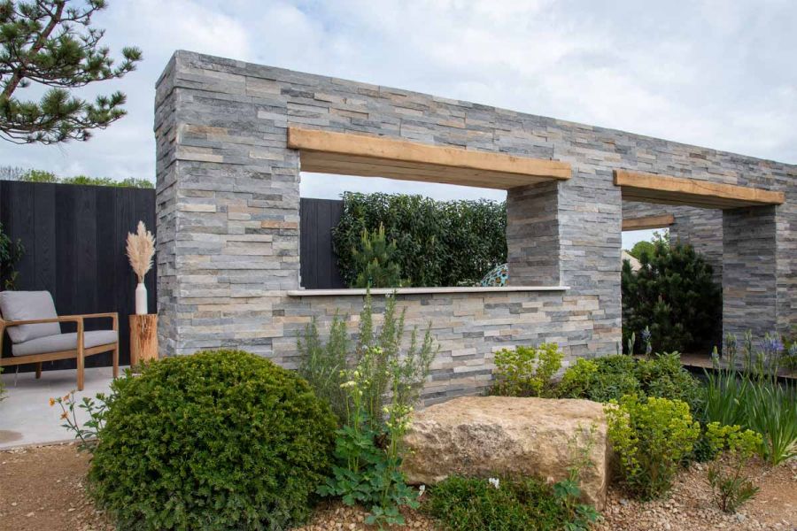 Graphite Sandstone Cladding faces deep L-shaped monolithic block sitting astride pond in dry-planted show garden at RHS Malvern.