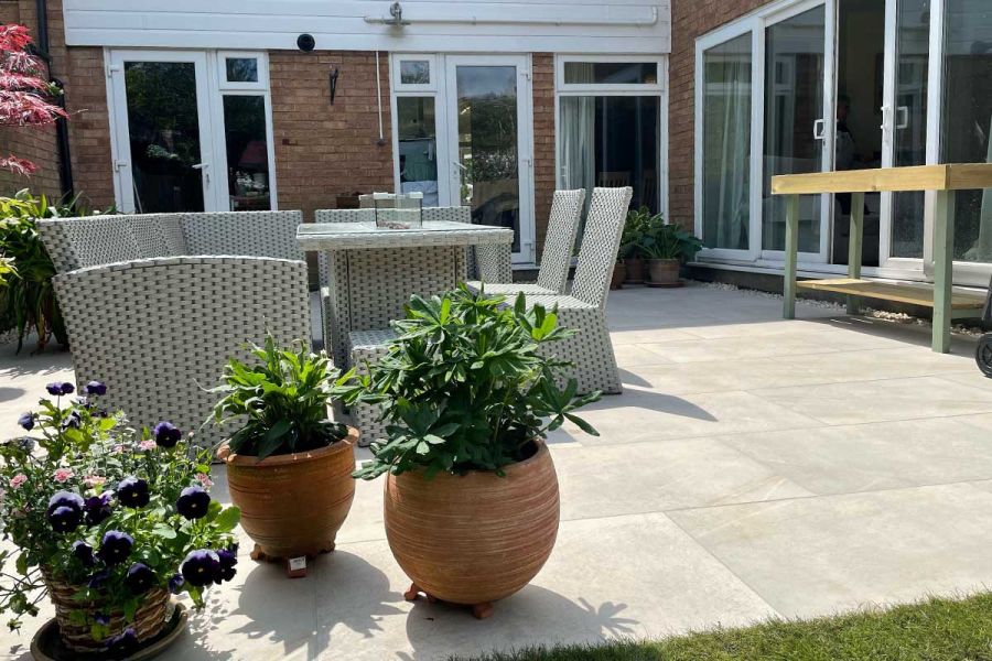 House with sliding doors opening out onto a large Ash Beige porcelain patio decorated with Terracotta pots and garden furniture.