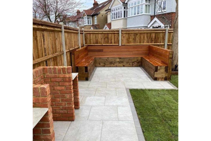 Small Steel Grey porcelain patio tiles edge rectilinear paved area in corner of fenced garden with inbuilt bench seating.