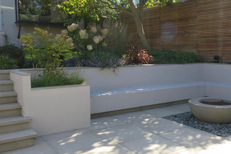 Cement Porcelain Paving garden featuring mature planting with trees, and a garden bench with a water feature in front.