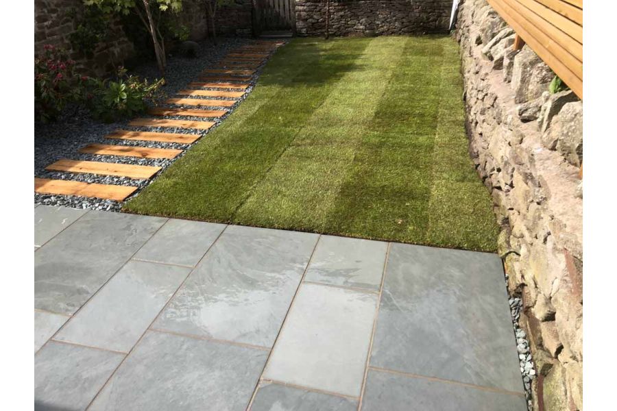 Rectangular lawn edged on 2 sides by path of planks set in gravel and patio of Brazilian Grey slate paving. Built by Green Bear.