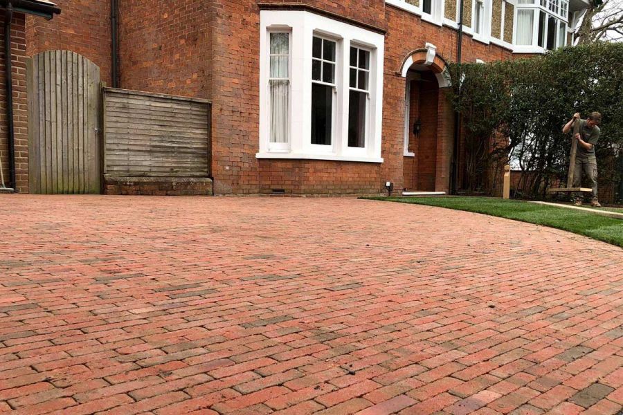 Large expanse of curve-edged driveway of Seville clay paving in front of semi-detached red brick period house. 