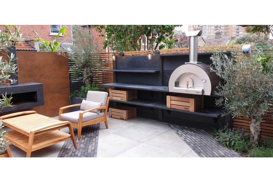 Black shelving with pizza oven sits on porcelain paving inset with Silver Grey Multi brick pavers. Design by Greenbird Gardening.