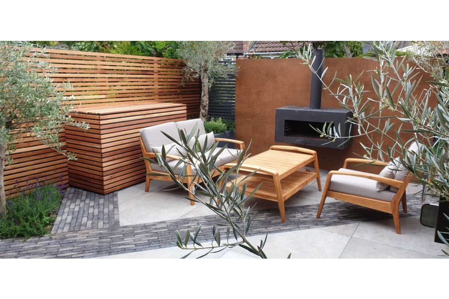 Outdoor lounge set and black stove on grey paving with stripes of Silver Grey Multi Clay Pavers. Design by Greenbird Gardening.