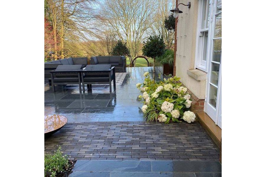 Silver Grey Multi clay paver strip leads between paving from french doors to bowl water feature on raised patio with lounge set.