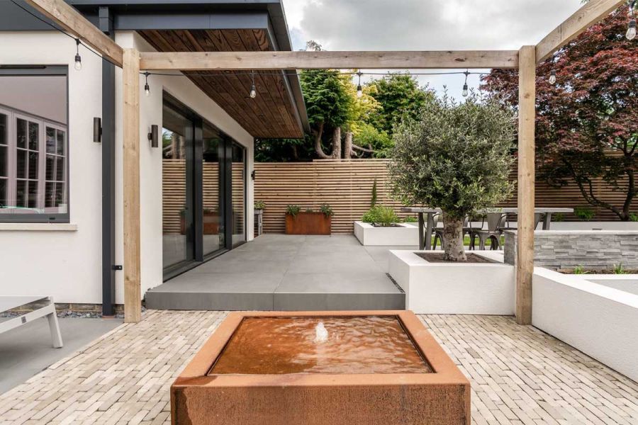 Square Corten steel raised pond with fountain on Gromo Antica clay pavers next to grey porcelain slabs. Design by Gadsden Gardens.