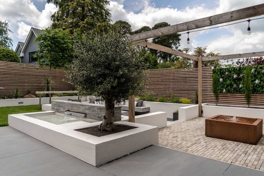 Gromo Antica buff clay paving with large format porcelain slabs in design with olive tree and sunken seating by Gadsden Gardens.