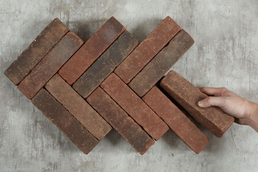 Hand places single Antique Red clay paver against 11 laid herringbone on light background. Free UK delivery available.