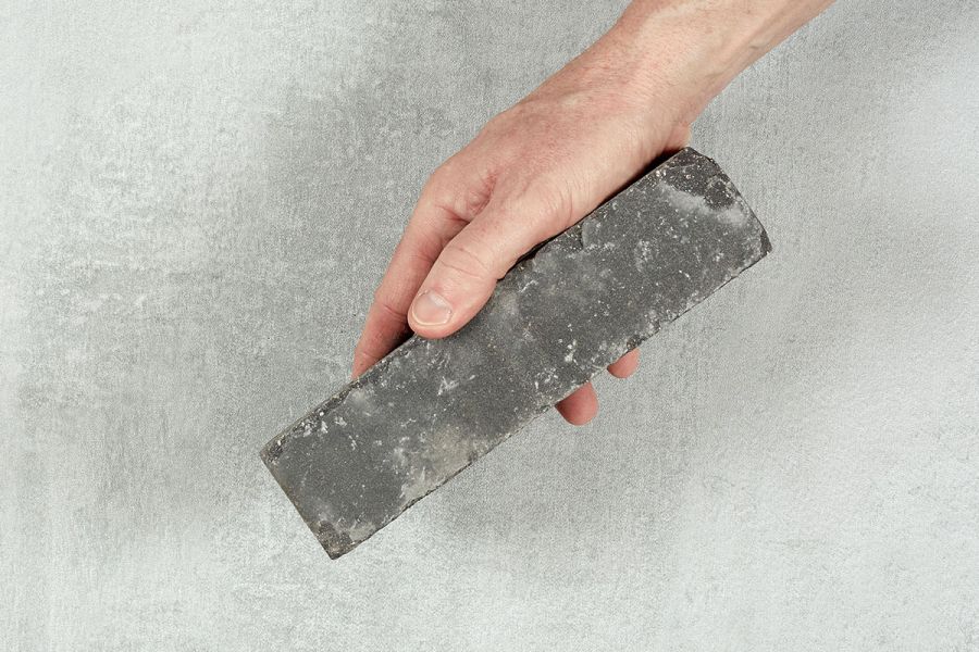 A hand holds a single dun-coloured Lucca clay paver against a light background. Free UK next-day delivery available. 