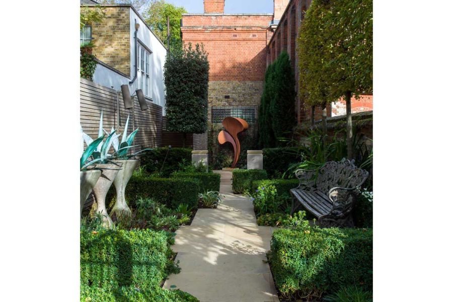Long narrow urban garden with clipped hedges, iron bench and Britannia Buff irregular-width path to distant sculpture.