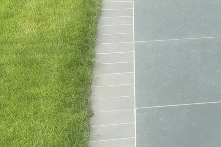 Platinum Grey setts edge darker grey porcelain patio tiles, separating them from a lawn. Laid by Healey Paving Services.
