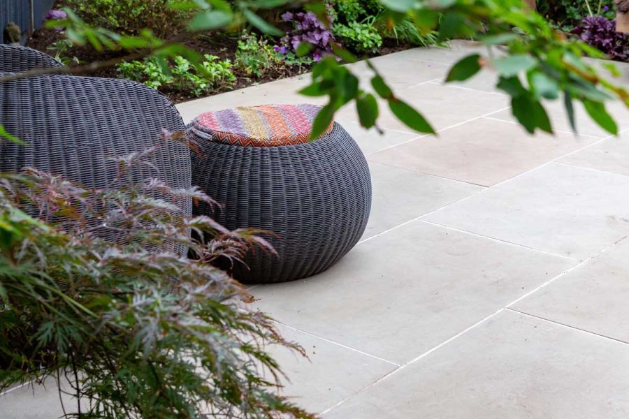 Dark rattan seat and footstool on Heath sawn sandstone patio with planted borders. Design by Daniel Shea. Built by Acacia Gardens.