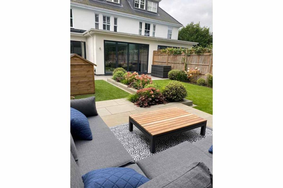 Outdoor coffee table sits on patterned tiles set into Heath Smooth Sandstone paving, in garden designed by Landscape Artisan.