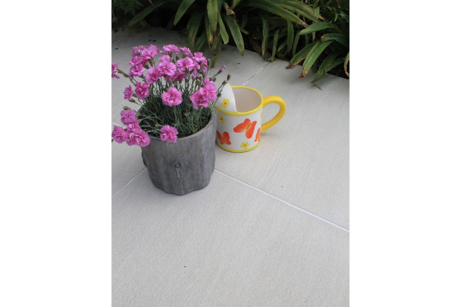 A small carnation-filled planter and ceramic watering can stand on Sandy White Porcelain Tiles with narrow joint of pale grout.
