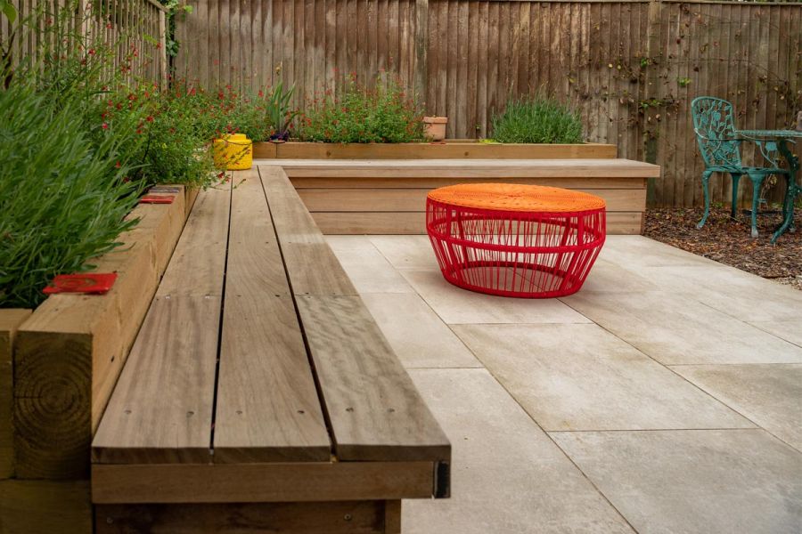 Hardwood L shaped garden bench with raised timber beds behind it and Cream porcelain paving on the floor in front.