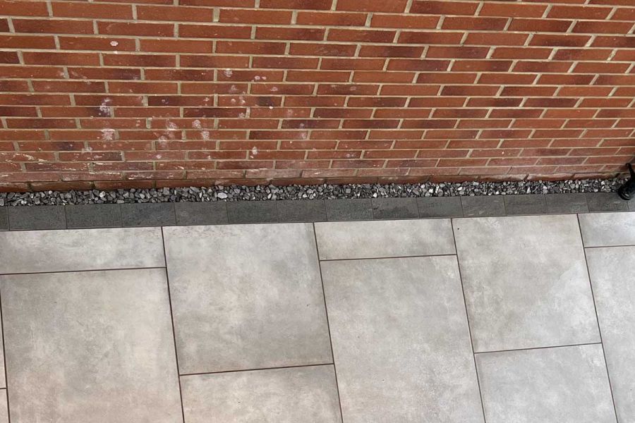 Platinum Grey porcelain setts edge grey paving next to brick wall, with gravel at base. Built by Instant Scenery.