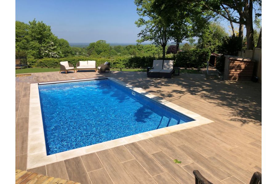 Swimming pool on a hot summers day with Rovere wood effect porcelain paving laid around looking out across beautiful countryside.