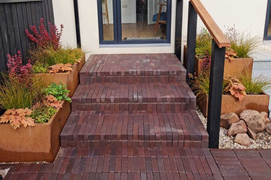 3 steps in Bolzano clay pavers and handrail rise to glass door between planters. Design by Jane Houghton. Built by Landigo Ltd.