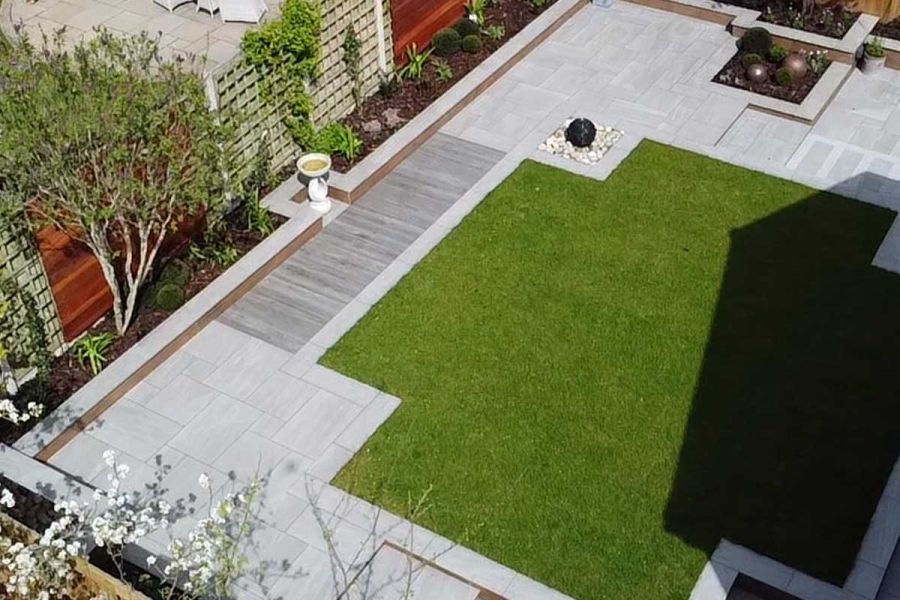 Birds eye view of a rear garden area showing an artificial lawn surrounded on all sides with various styles of porcelain paving.