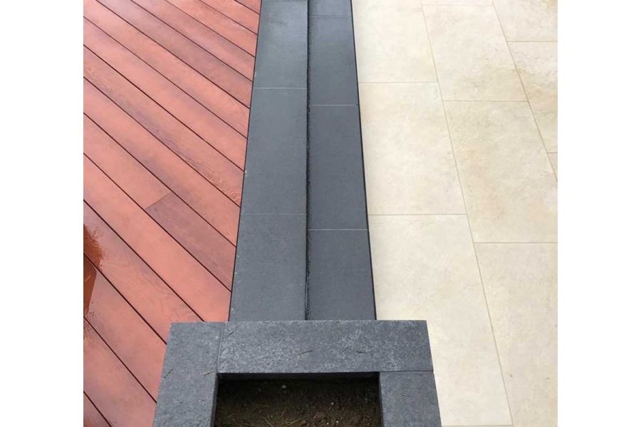 Line of dark grey narrow slabs separate areas of cream coloured porcelain paving and Jarrah Millboard decking laid at an angle.
