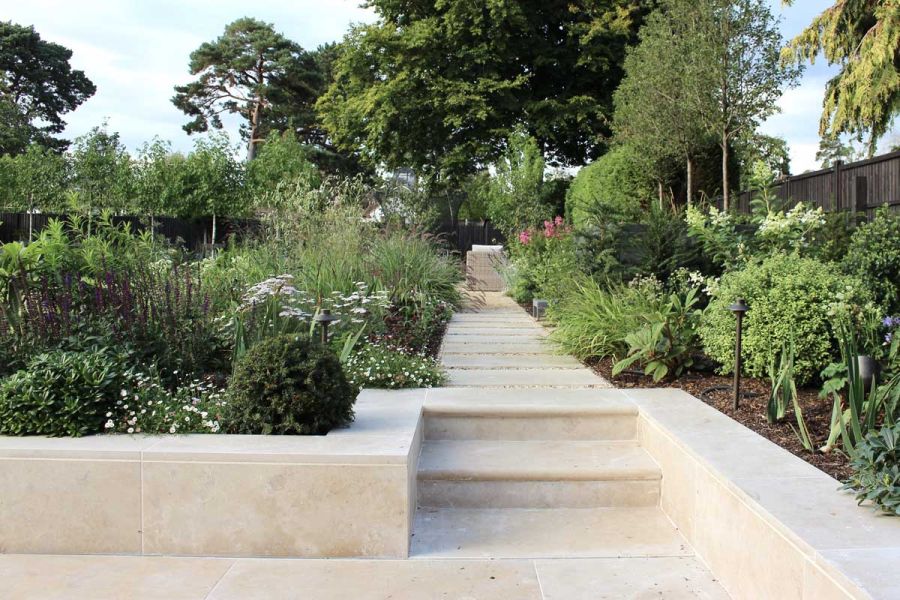 2 bullnose steps rise from patio to long straight path between planted beds. All in Jura Beige limestone. Design by Jen Berry.