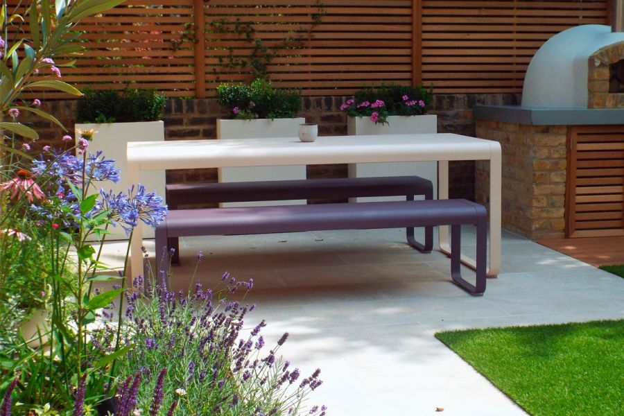 Gea porcelain patio featuring white dining table with purple benches, white fibreglass tall trough planters beautifully planted.