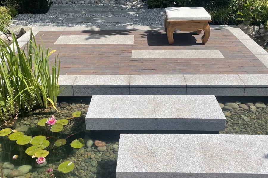 2 granite stepping stones lead to Chelsea Clay paved area floating above pond at Gardeners World live 2022. Design by JKD Studio.