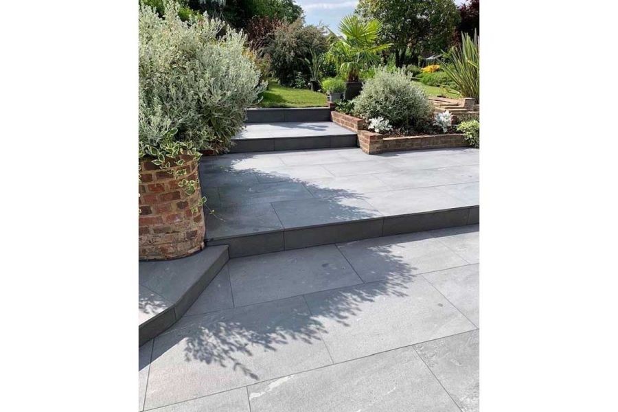 Platinum Grey Porcelain patio on multiple platforms stepping up towards a lawn and heavily planted garden area.