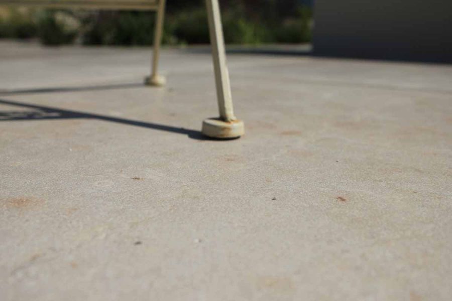 Close view of feet of metal outdoor chair on Jura Beige smooth limestone slabs, showing textures and tones of paving.