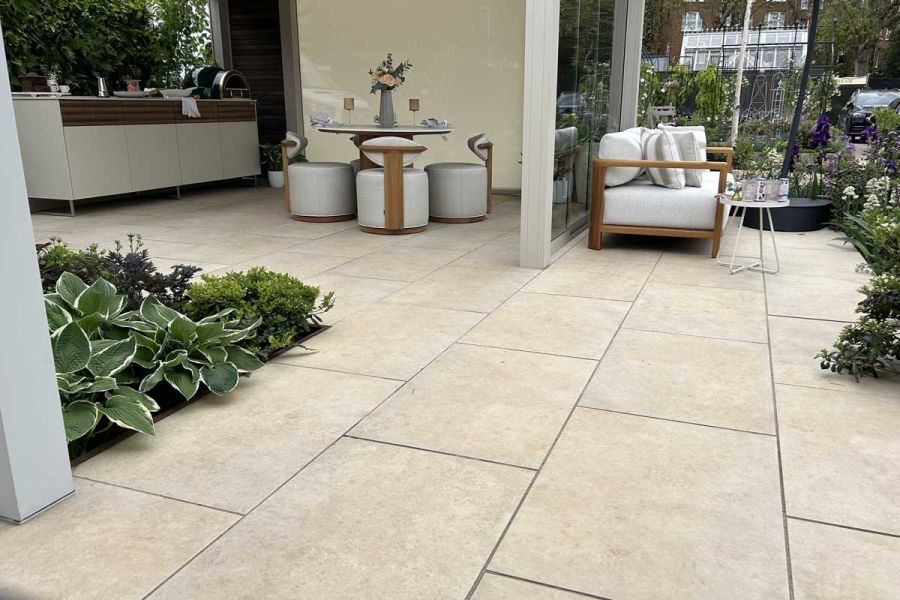 Large Jura Beige Porcelain patio area grouted with dark grey exterior grout and featuring outdoor seating, dining and kitchen area.