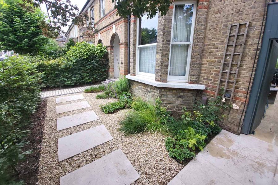 Front garden of period terrace house, with shrub border and gravel set with widely separated Jura Beige sawn limestone slabs.