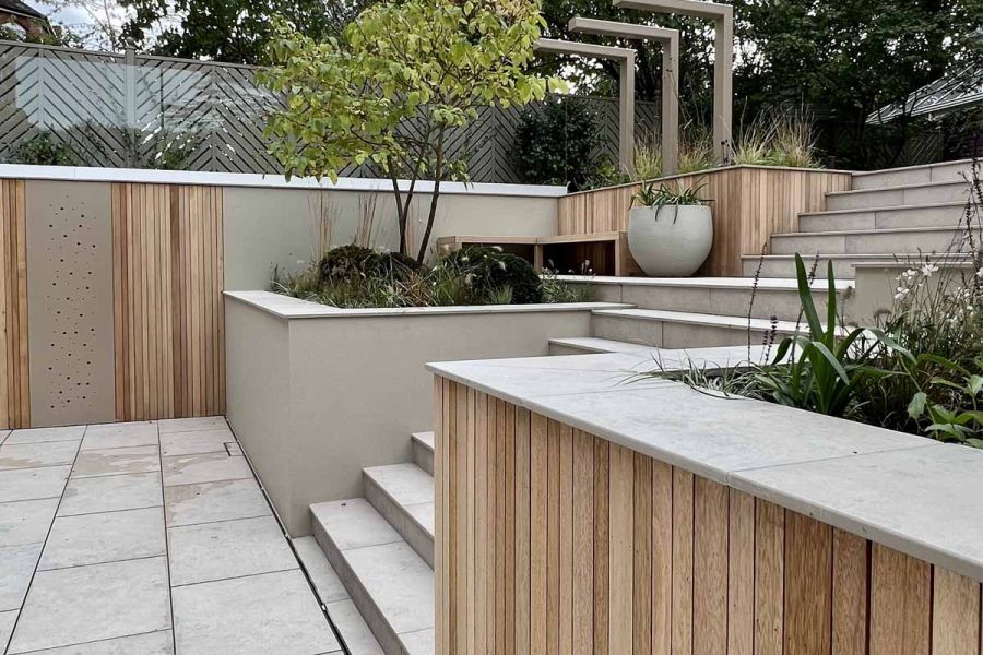 2 widths of Jura Grey porcelain smooth coping top a 2 sides of wood-clad raised bed, creating a wide section for seating.