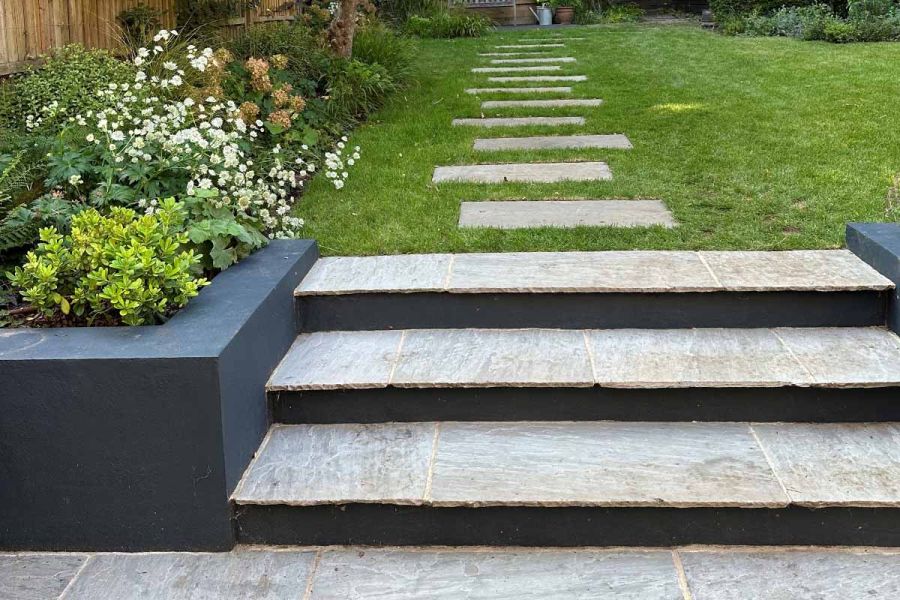Kandla Grey sandstone slabs, in staggered line, create stepping stone path in grass, leading from 3 matching steps to end of garden.