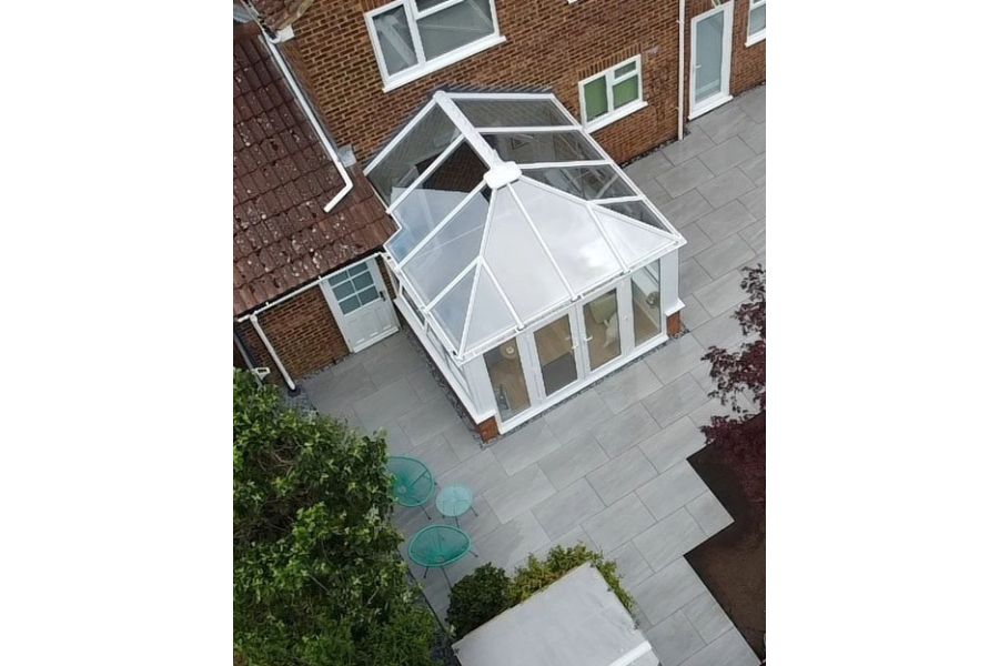 Aerial view of conservatory attached to house surrounded by Kandla Grey outdoor porcelain tile patio, edged with trees and shrubs.