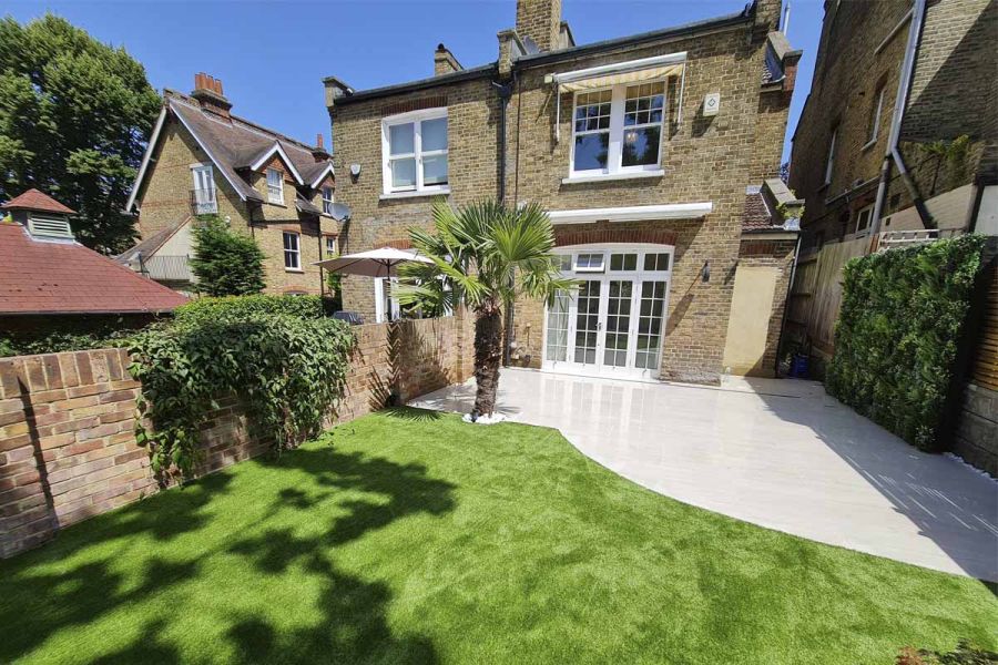 Kandla Grey Porcelain patio with curved edges and tree fern separates rear of Victorian semi-detached from lush lawn.