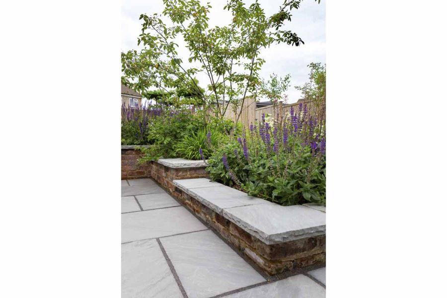 Kandla Grey Indian sandstone coping stones, with hand-cut, rock-faced edge profile, on broad brick walls retaining flower beds.