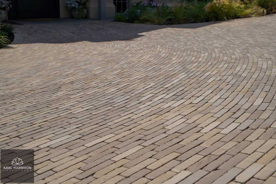 Huge area of Gromo Antica clay pavers laid in curved pattern leading to front of house in deep shadow. Designed by Karl Harrison.
