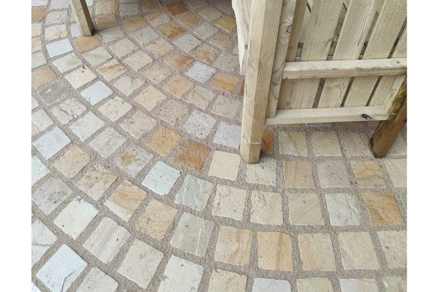 Legs of wooden furniture sit on mint sandstone setts with curved paving pattern and thick joints in design by Katerina Kantalis.