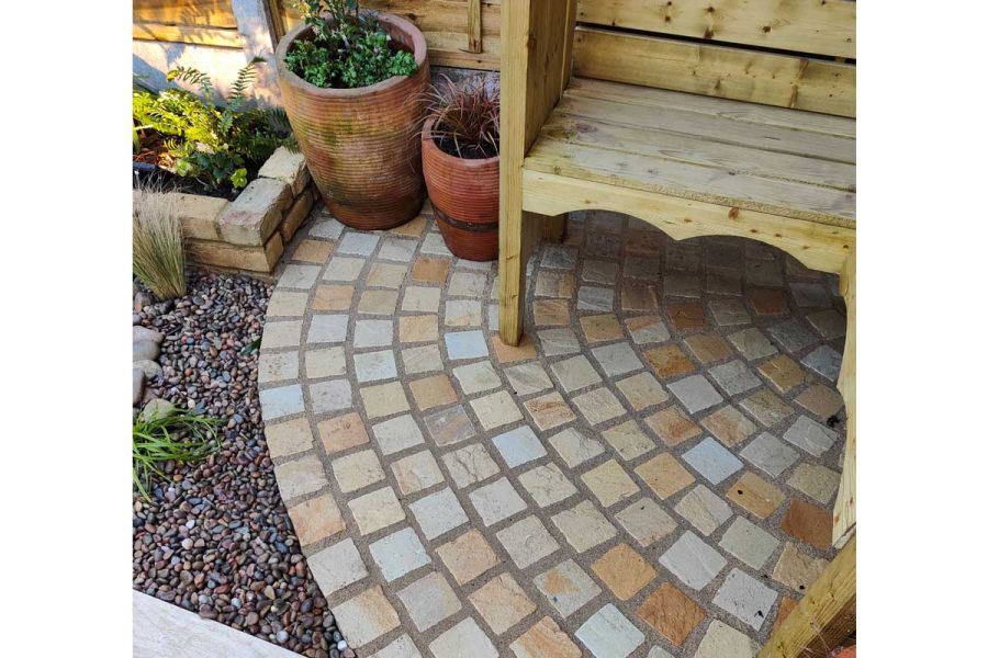 Mint sandstone setts, in range of buffs, yellows and creams, laid in curved rows under wooden bench. Design by Katerina Kantalis.